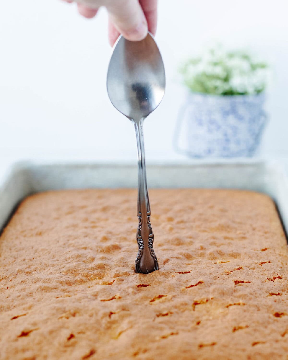 A spoon poking holes into a cake.