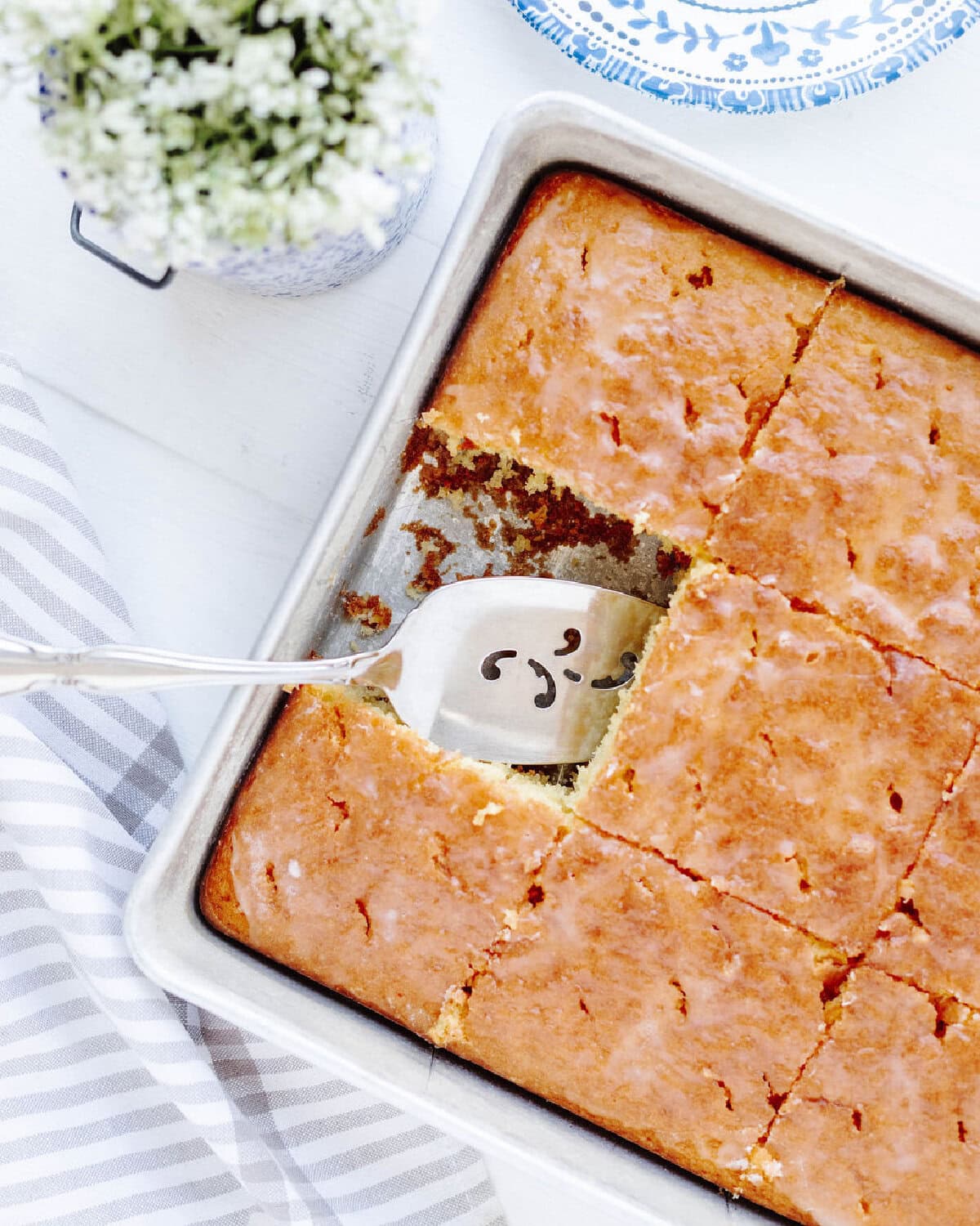 A baked lemon cake with a slice served using a spatula.