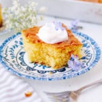 A slice of lemon poke cake garnished with a dollop of whipped cream on a plate.