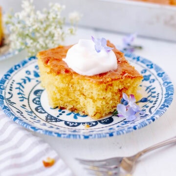 A slice of lemon poke cake garnished with a dollop of whipped cream on a plate.