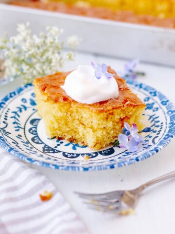 A slice of lemon poke cake garnished with a dollop of whipped cream on a plate.