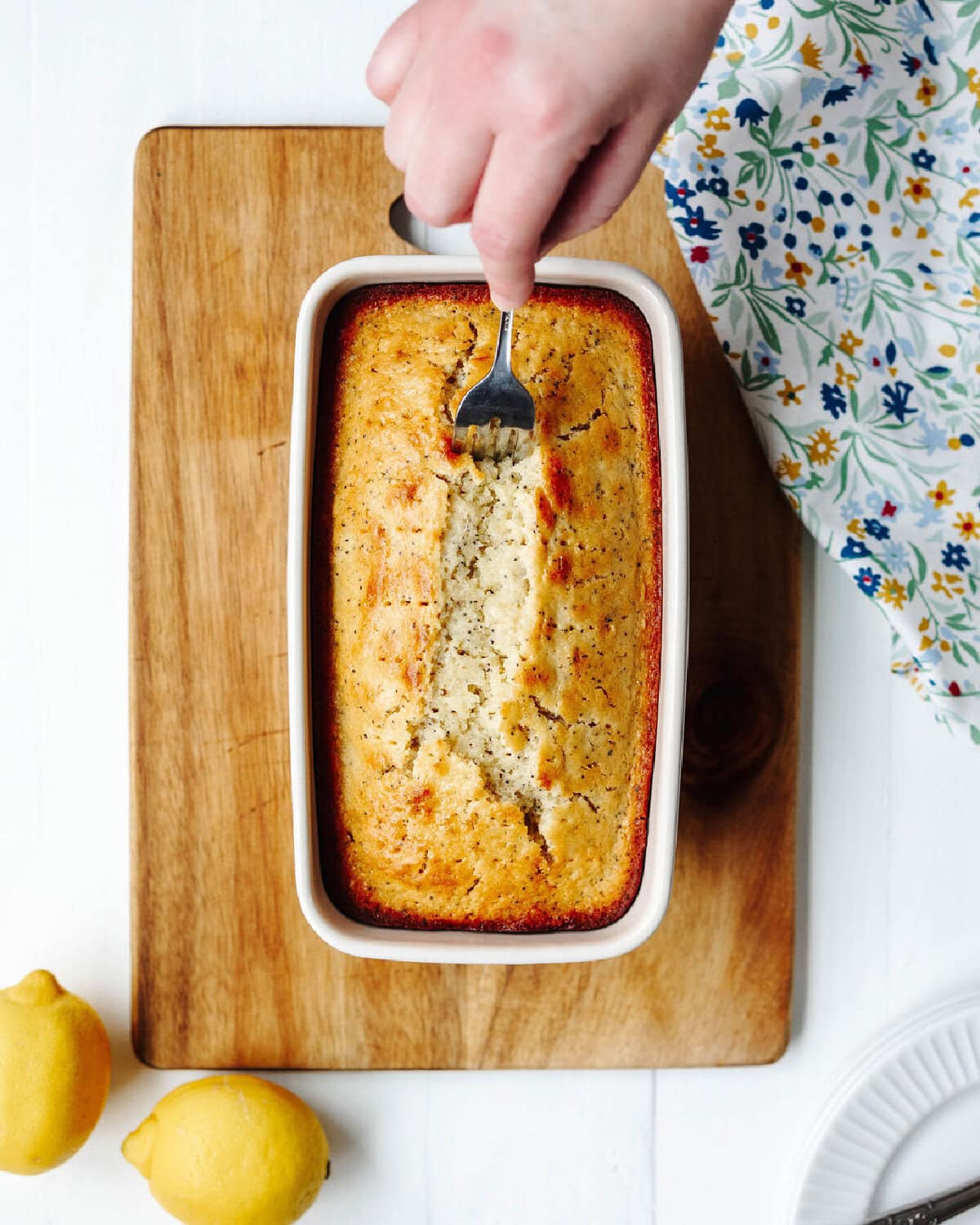A fork poking holes into lemon poppyseed bread to pour the glaze into.