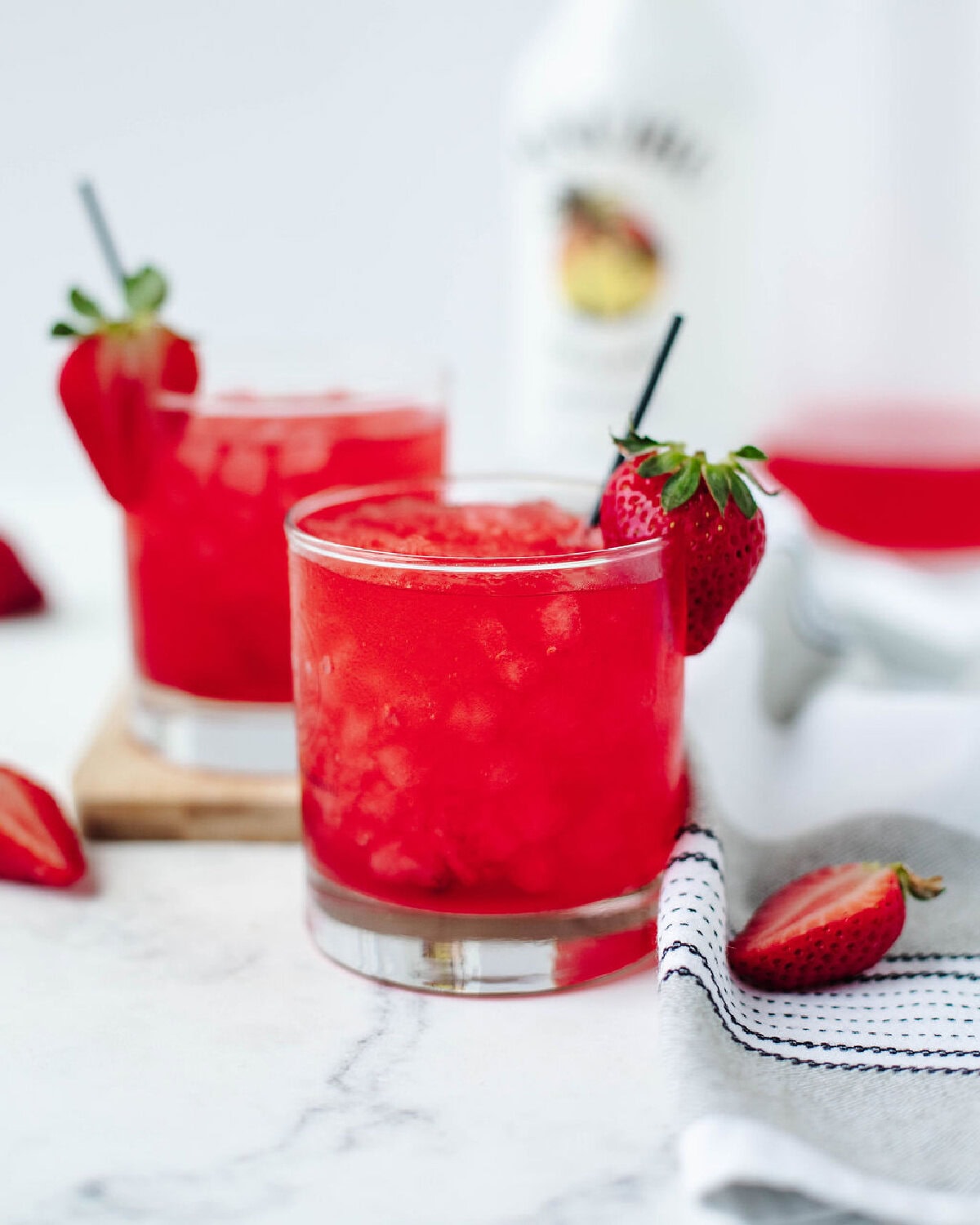 Poured skittles cocktail in a glass with a sliced strawberry rim.