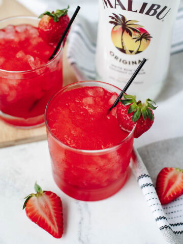 Liquid Skittles Cocktails in glasses with a strawberry on the rim.