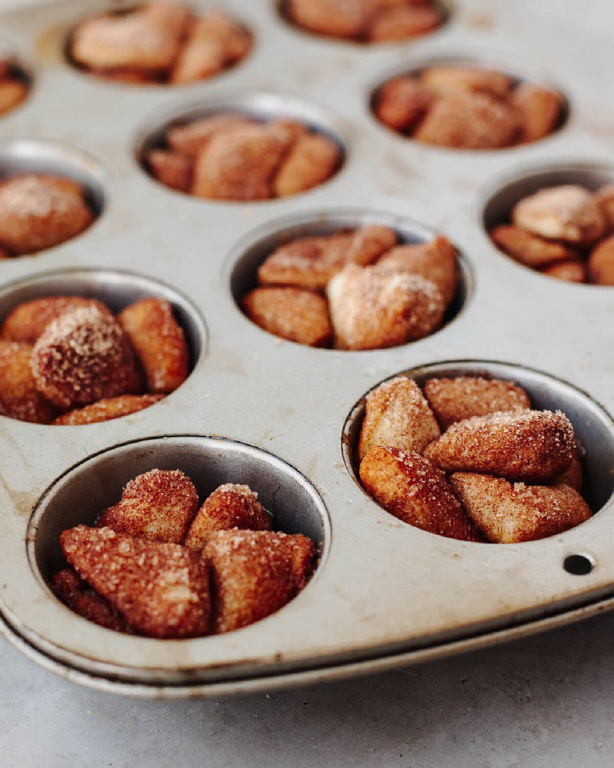 monkey bread dough pieces in muffin tin before baking with cinnamon sugar.