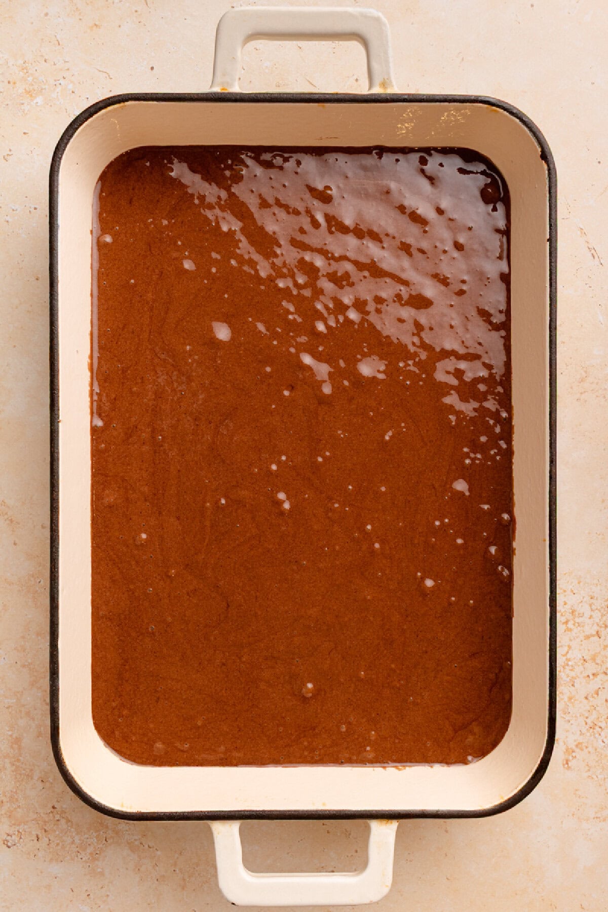 Chocolate cake batter spread into a prepared 9x13 baking pan.