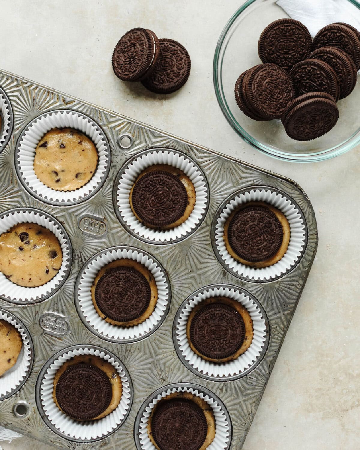 An Oreo placed on top of cookie dough in a muffin cup.