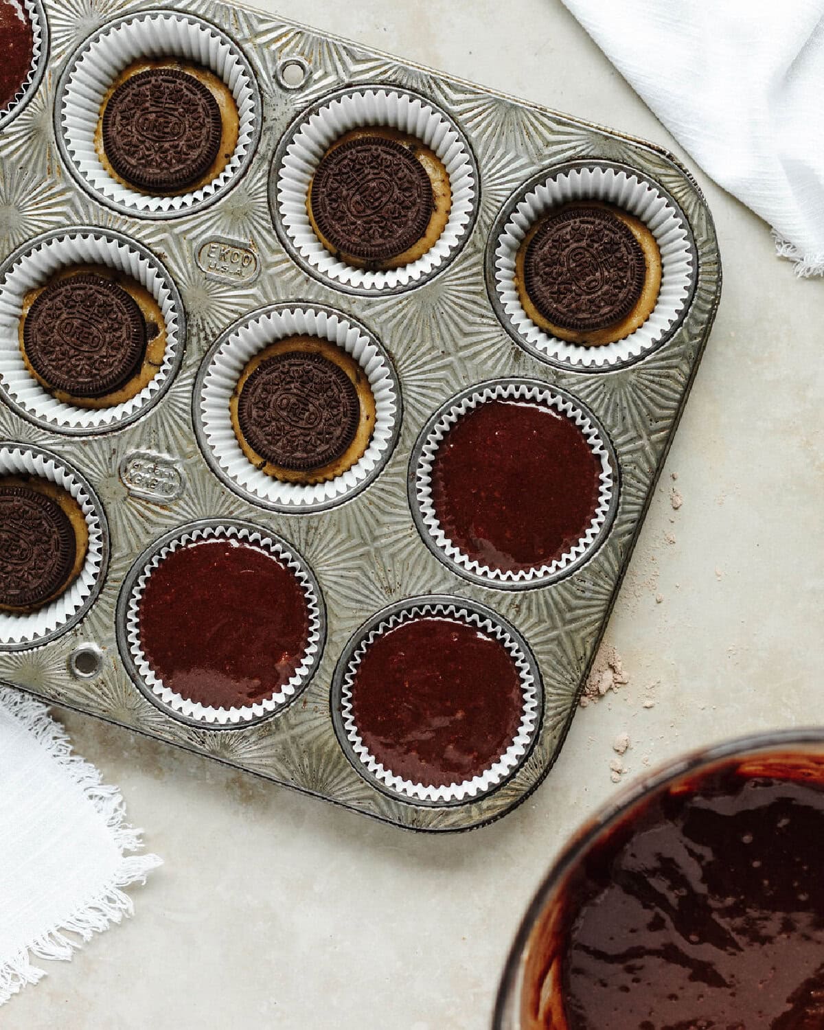 Brownie batter poured on top of an Oreo and cookie dough in a paper lined muffin tray.