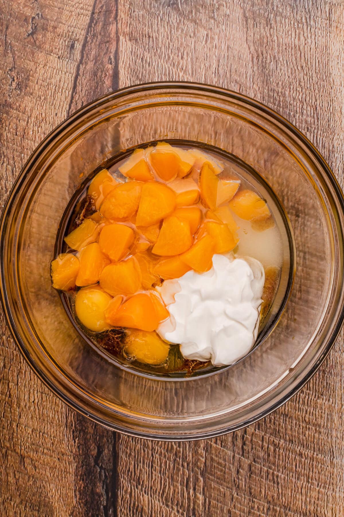 Peaches, sugar, sour cream, and oil combined in a glass mixing bowl.