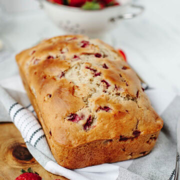 A baked loaf of strawberry bread on a wood cutting board ready to serve.