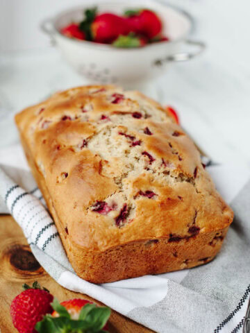 A baked loaf of strawberry bread on a wood cutting board ready to serve.