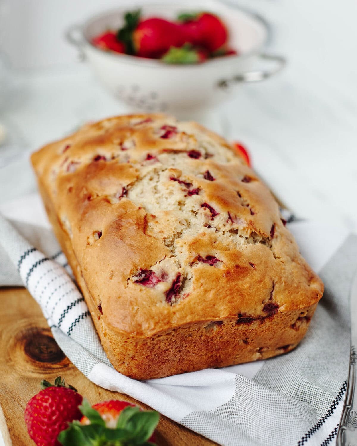 Moist strawberry bread loaf baked with fresh strawberries on a wooden cutting board.
