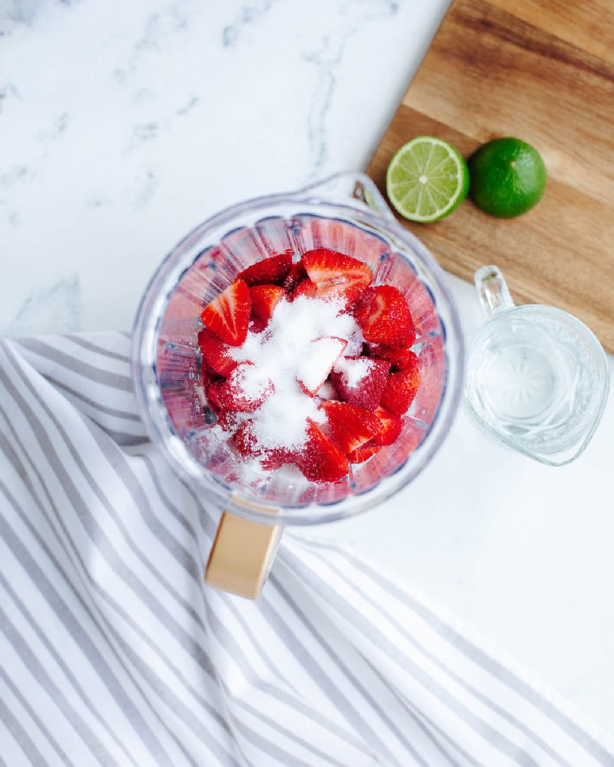 Fresh strawberries, sugar, and lime juice combined in a blender pitcher.