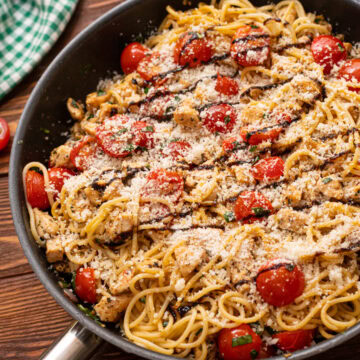 Bruschetta chicken pasta in a skillet with a balsamic glaze and Parmesan cheese.