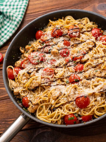 Bruschetta chicken pasta in a skillet with a balsamic glaze and Parmesan cheese.