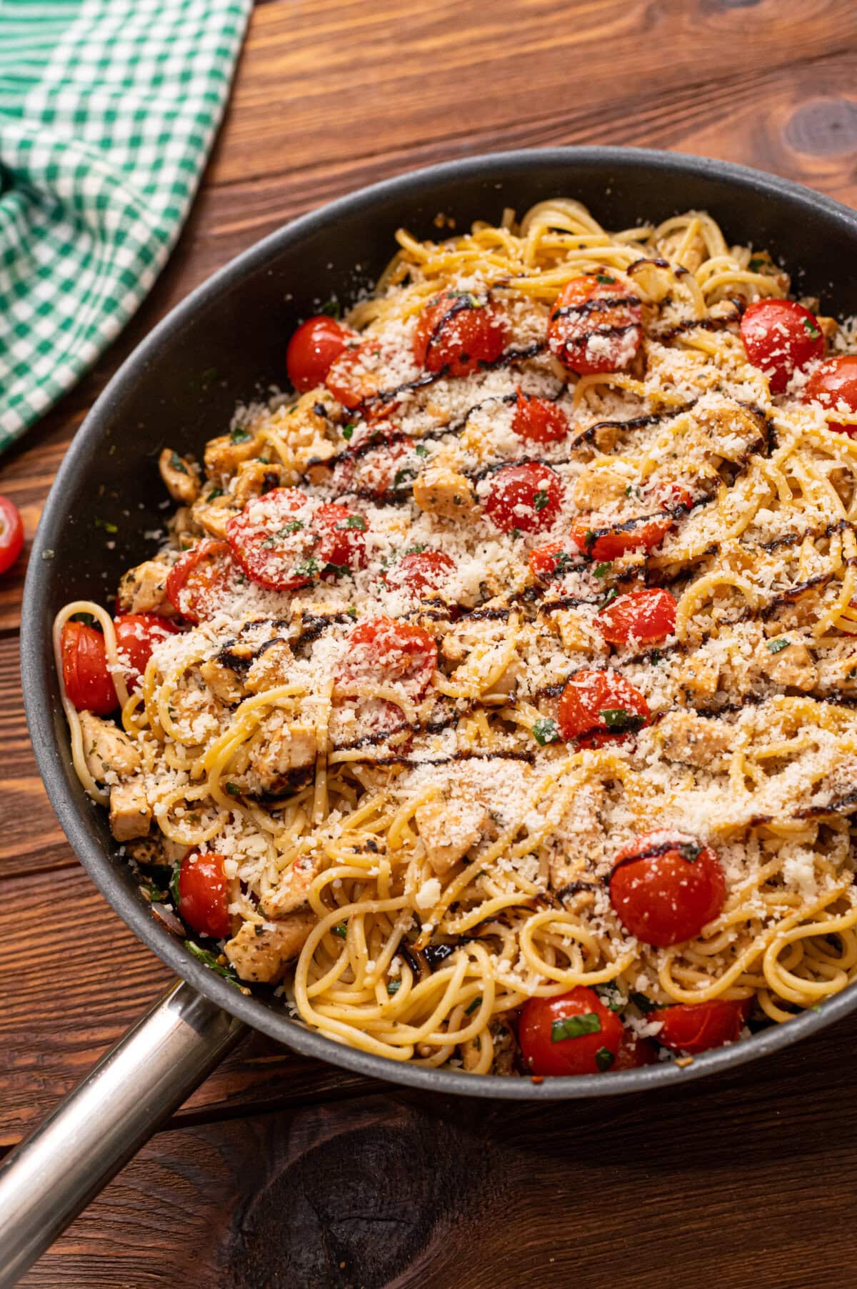 Bruschetta chicken pasta in a skillet with a balsamic glaze and Parmesan cheese.