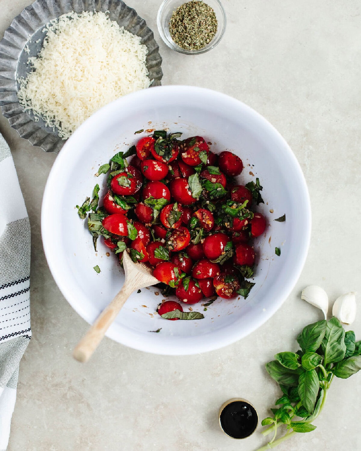 Cherry tomatoes, olive oil, and Basil combined in a white bowl.
