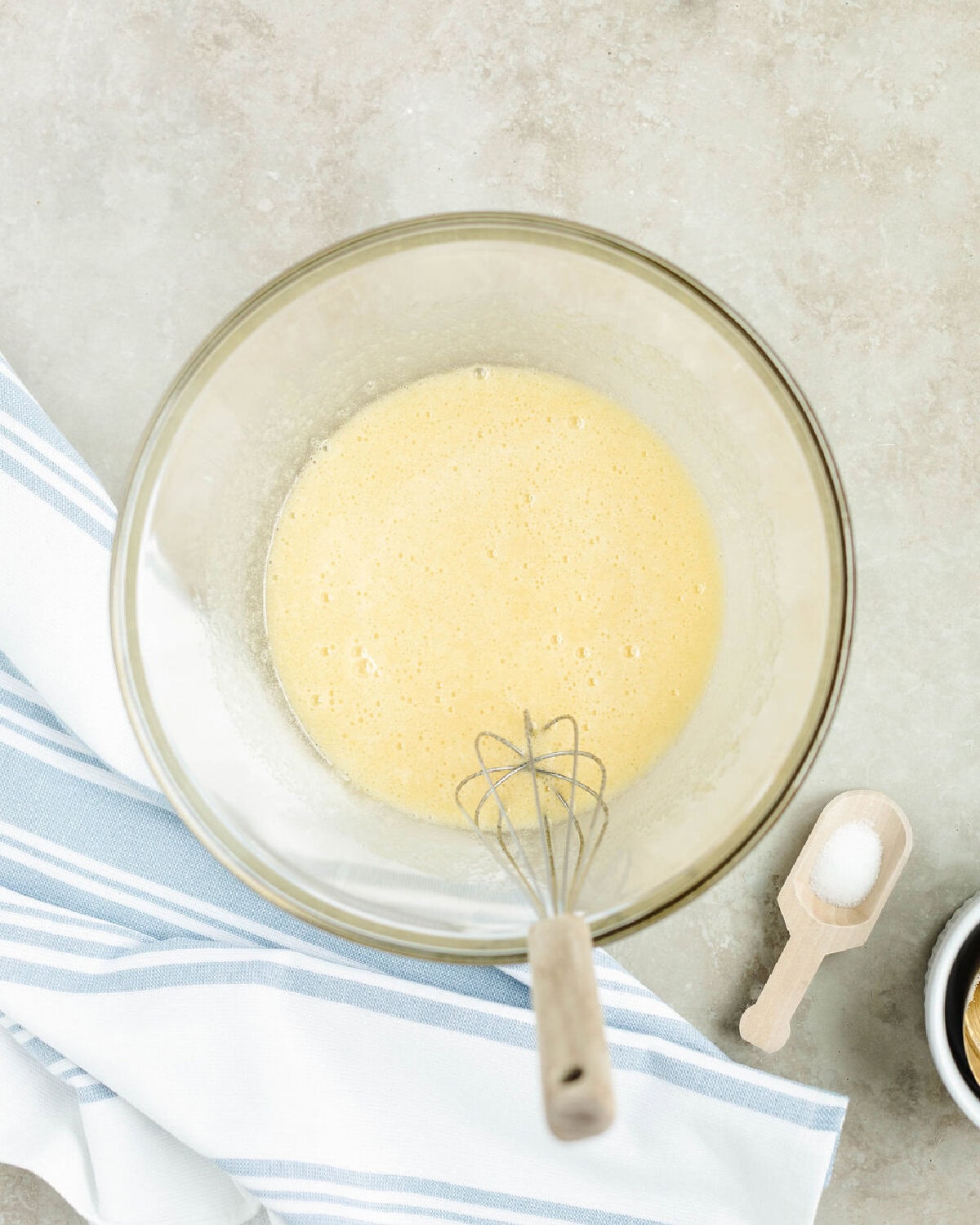 Sugar and eggs whisked together in a glass mixing bowl.