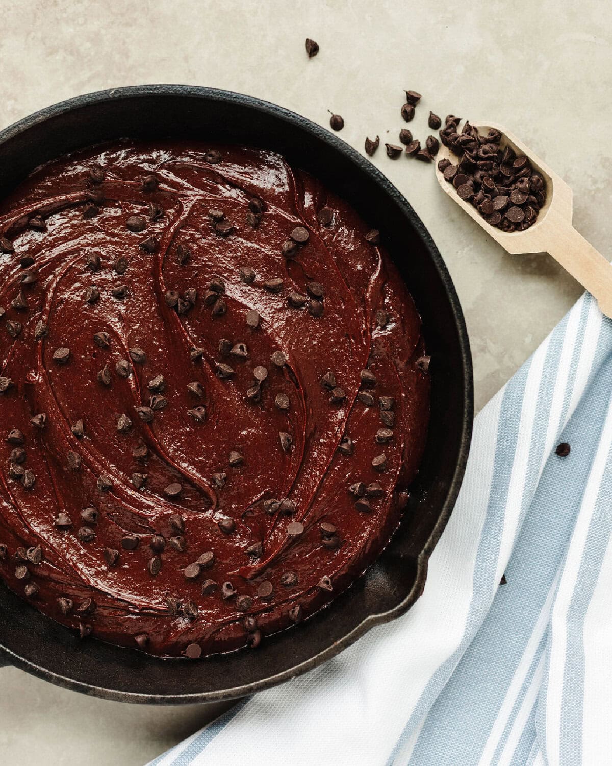 Chocolate brownie batter spread into a prepared cast iron skillet with chocolate chips sprinkled on top.