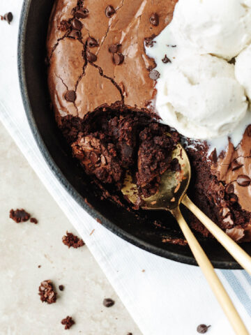 A spoon scooping brownies out of a cast iron skillet.