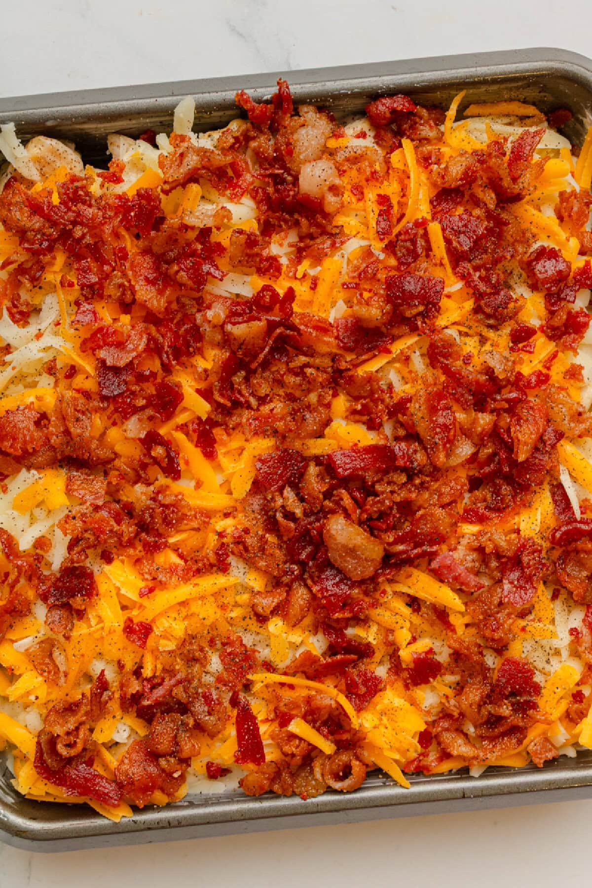Shredded cheeses on top of a chicken casserole in an 8x8 baking pan.