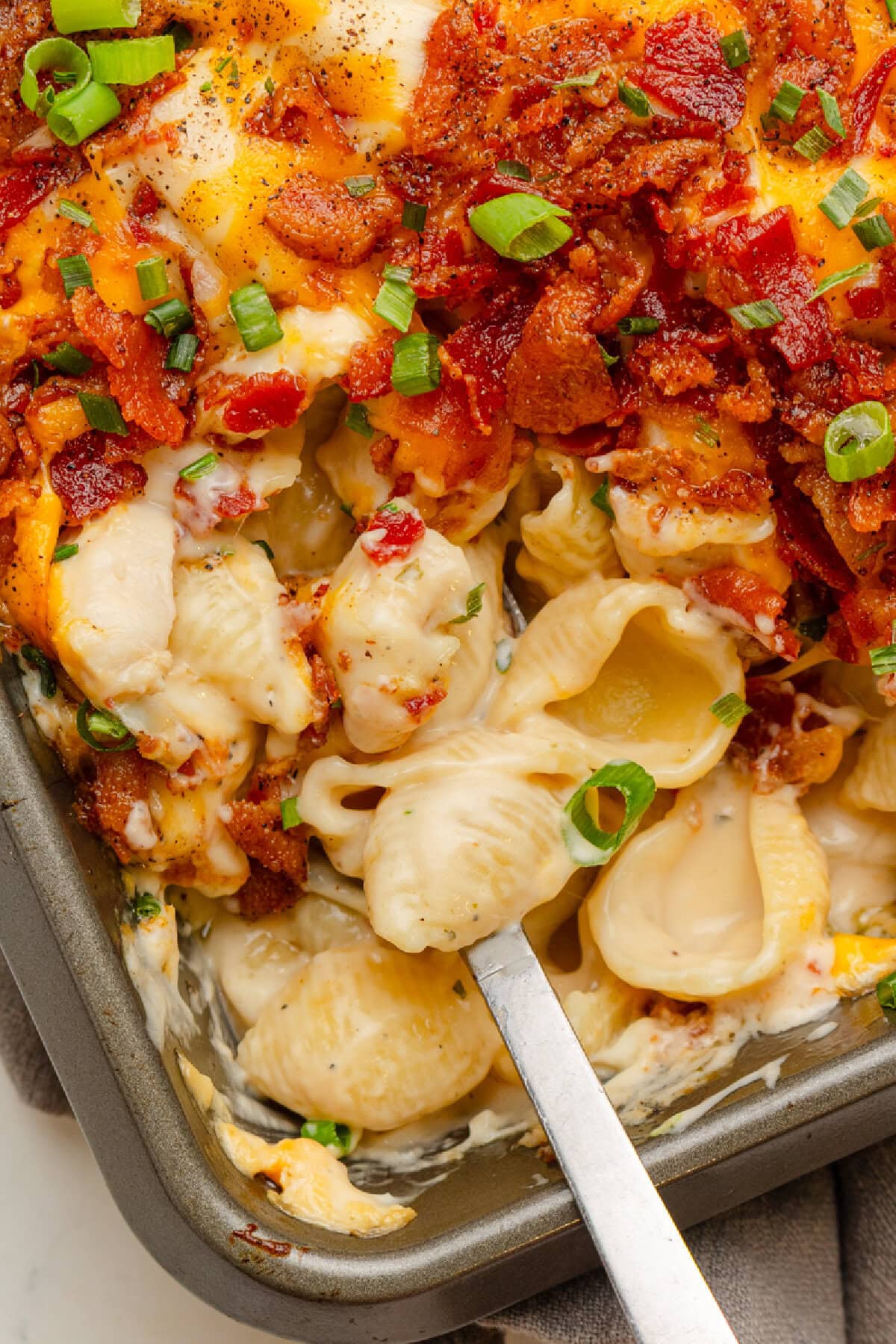 Creamy and cheesy chicken bacon Ranch casserole being served with a spoon from a baking pan.