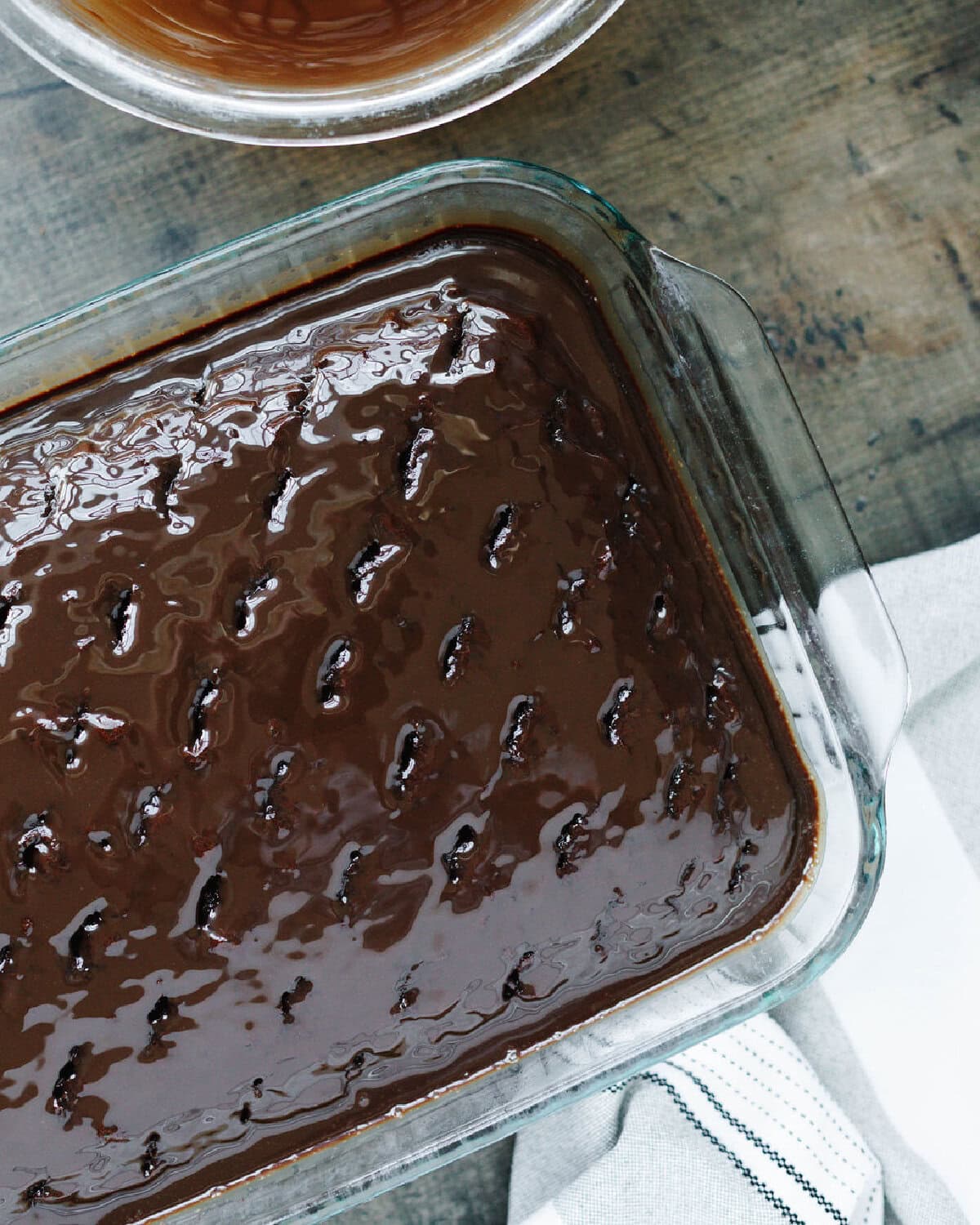 pouring chocolate mixture over poke cake.