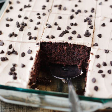 A serving spoon serving a piece of Kahlua poke cake from a baking pan.