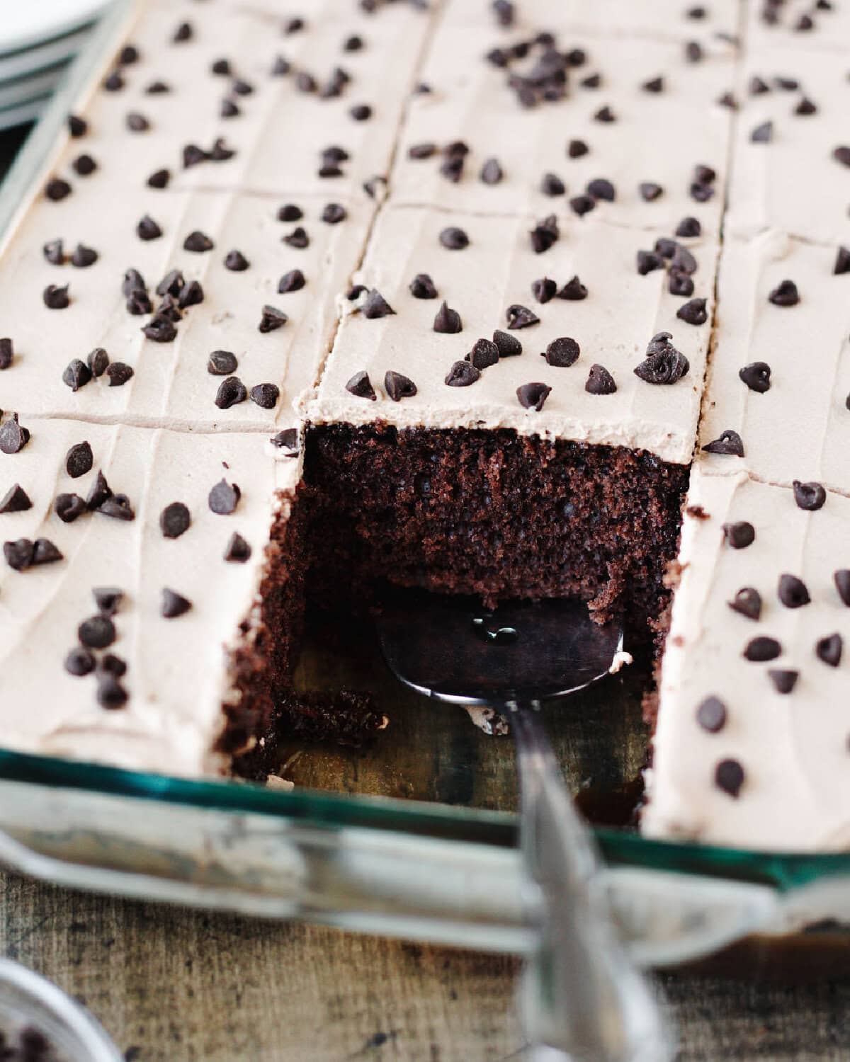 A serving spoon serving a piece of Kahlua poke cake from a baking pan.