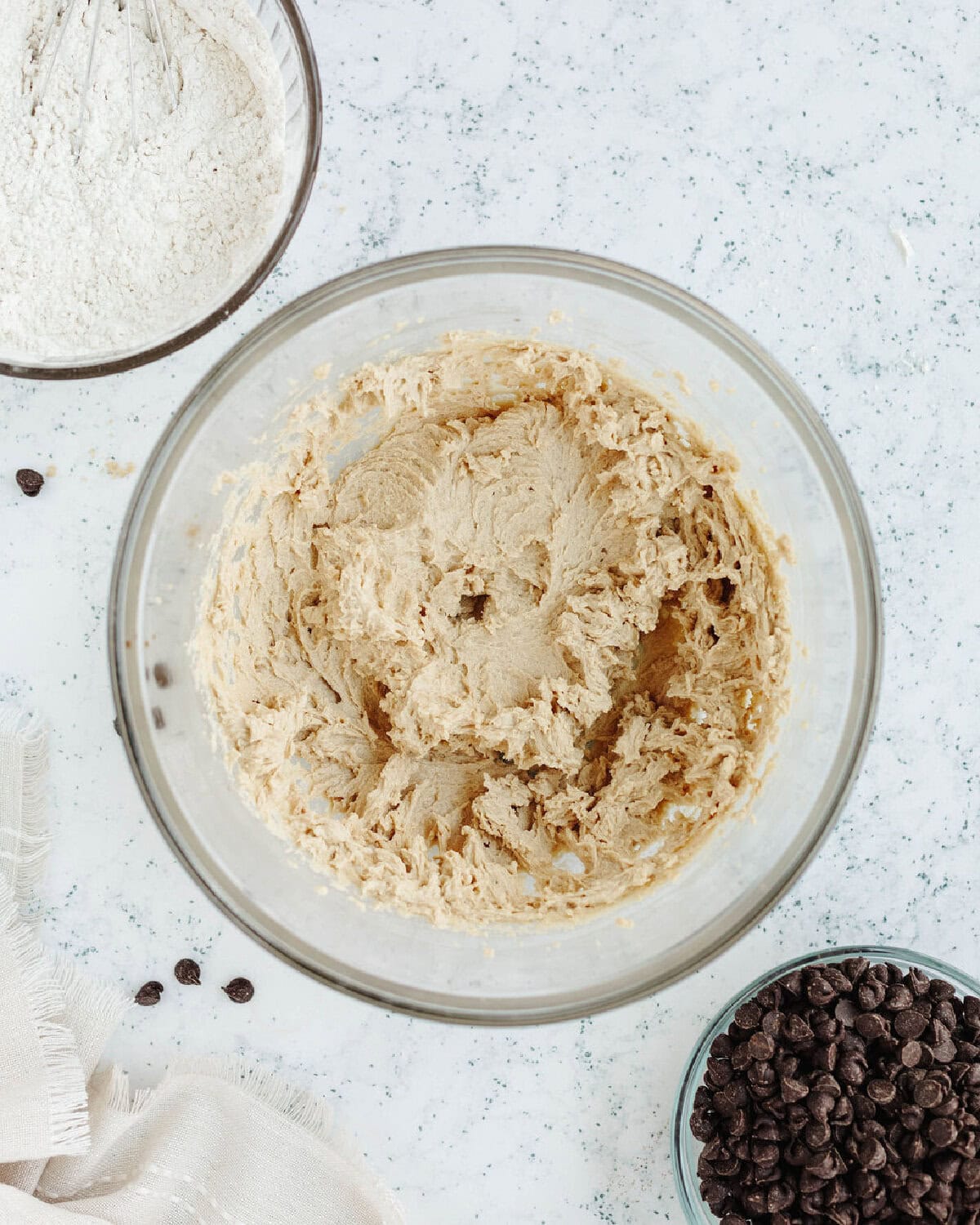Eggs and vanilla folded into cookie dough in a glass mixing bowl.