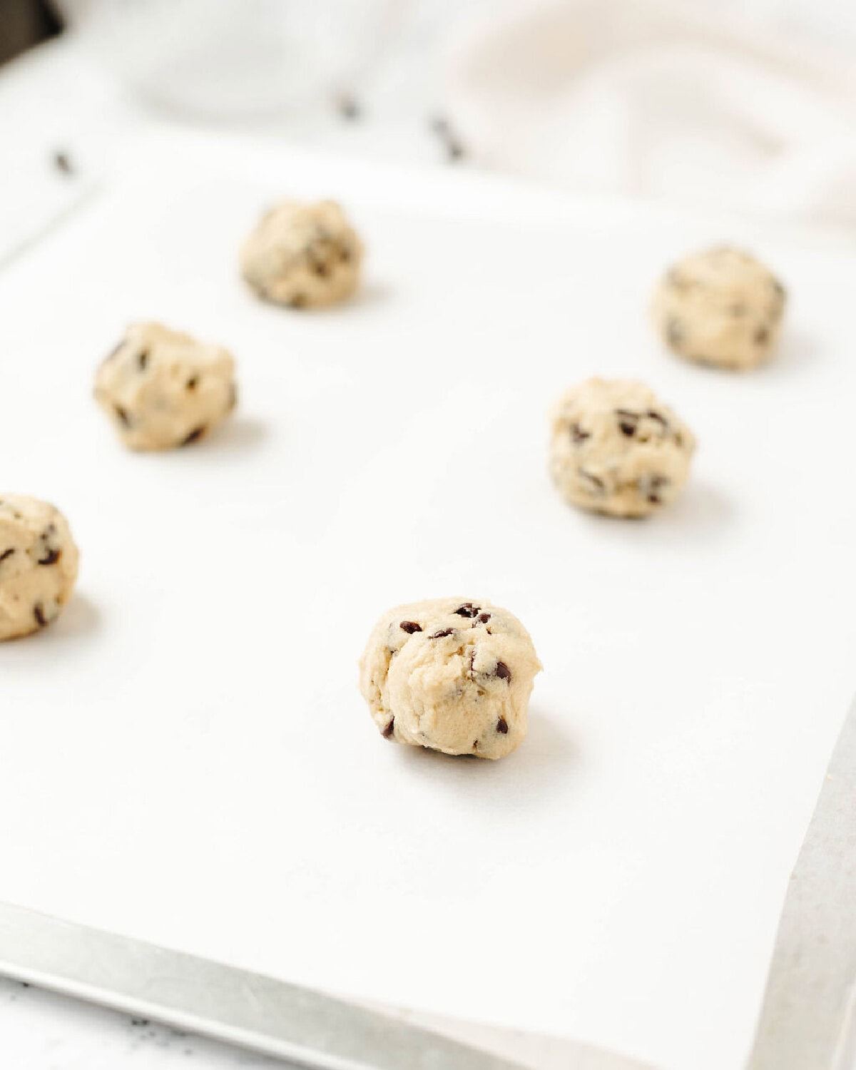 Chocolate chip cookie dough balls on a parchment lined baking sheet.