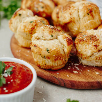 Mini garlic monkey bread baked and served on a wood serving board with dipping sauce.
