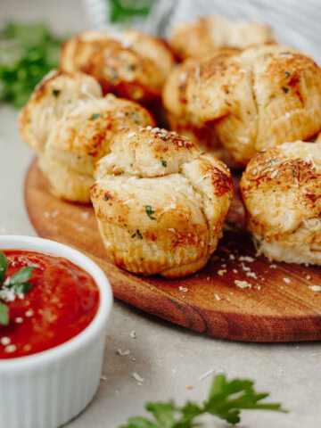 Mini garlic monkey bread baked and served on a wood serving board with dipping sauce.