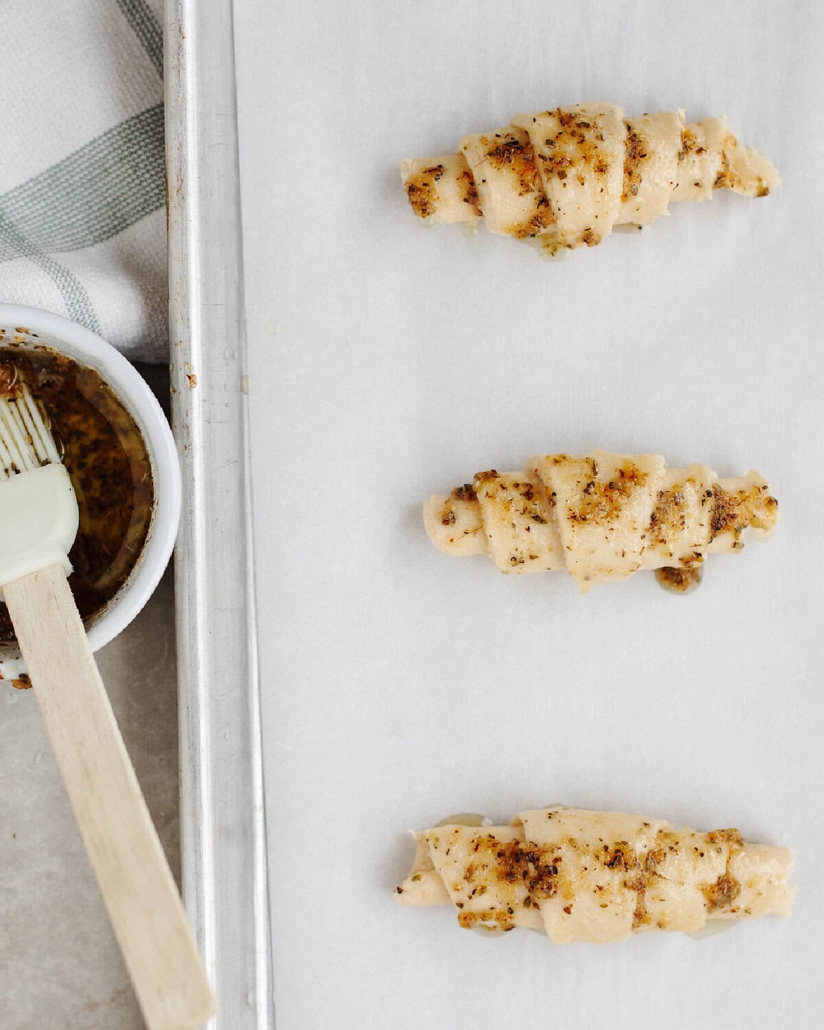Melted butter mixed with garlic powder and oregano brushed on top of unbaked crescents on a baking sheet.