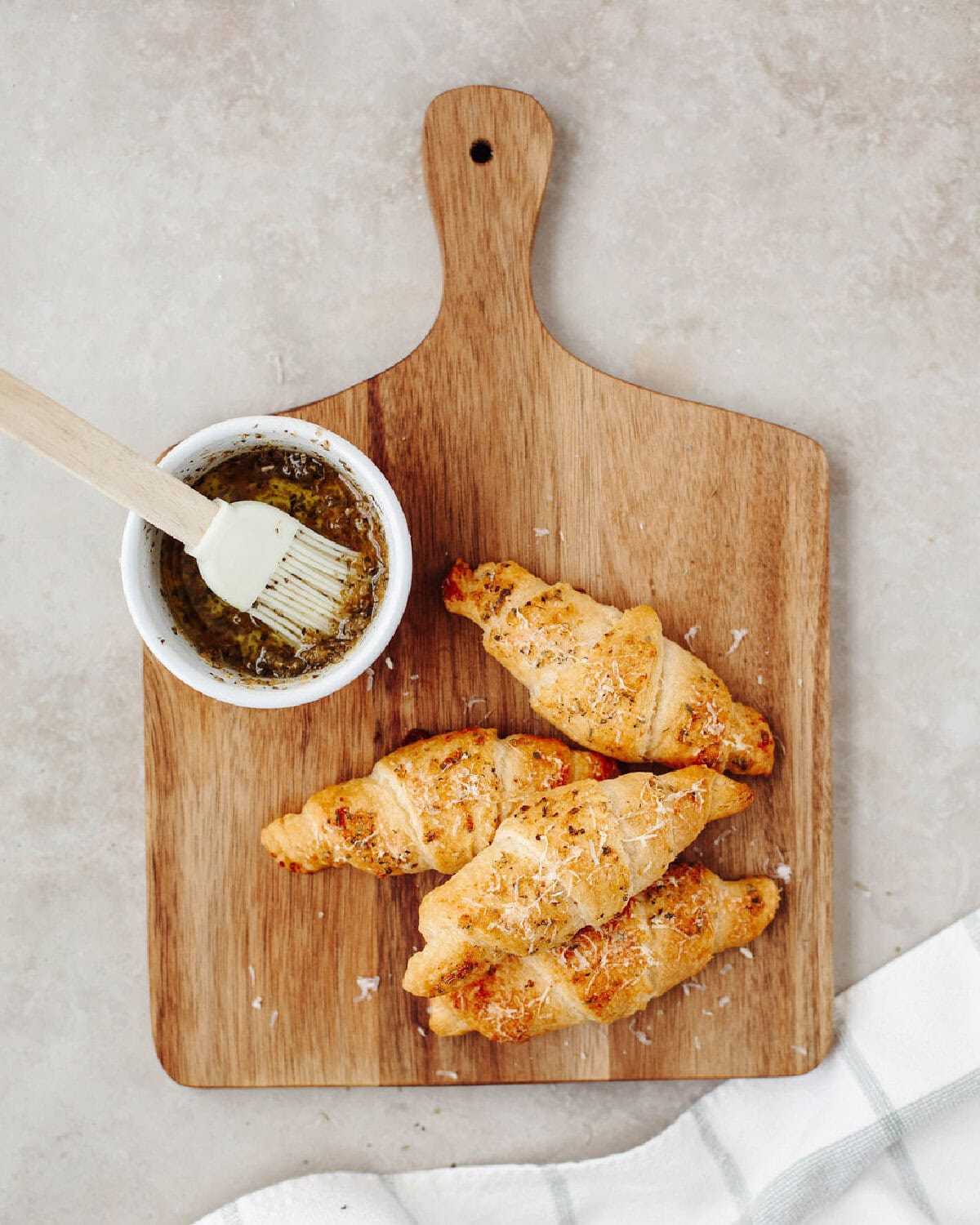 A melted butter mixture in a white bowl next to baked crescents with a seasoned coating.