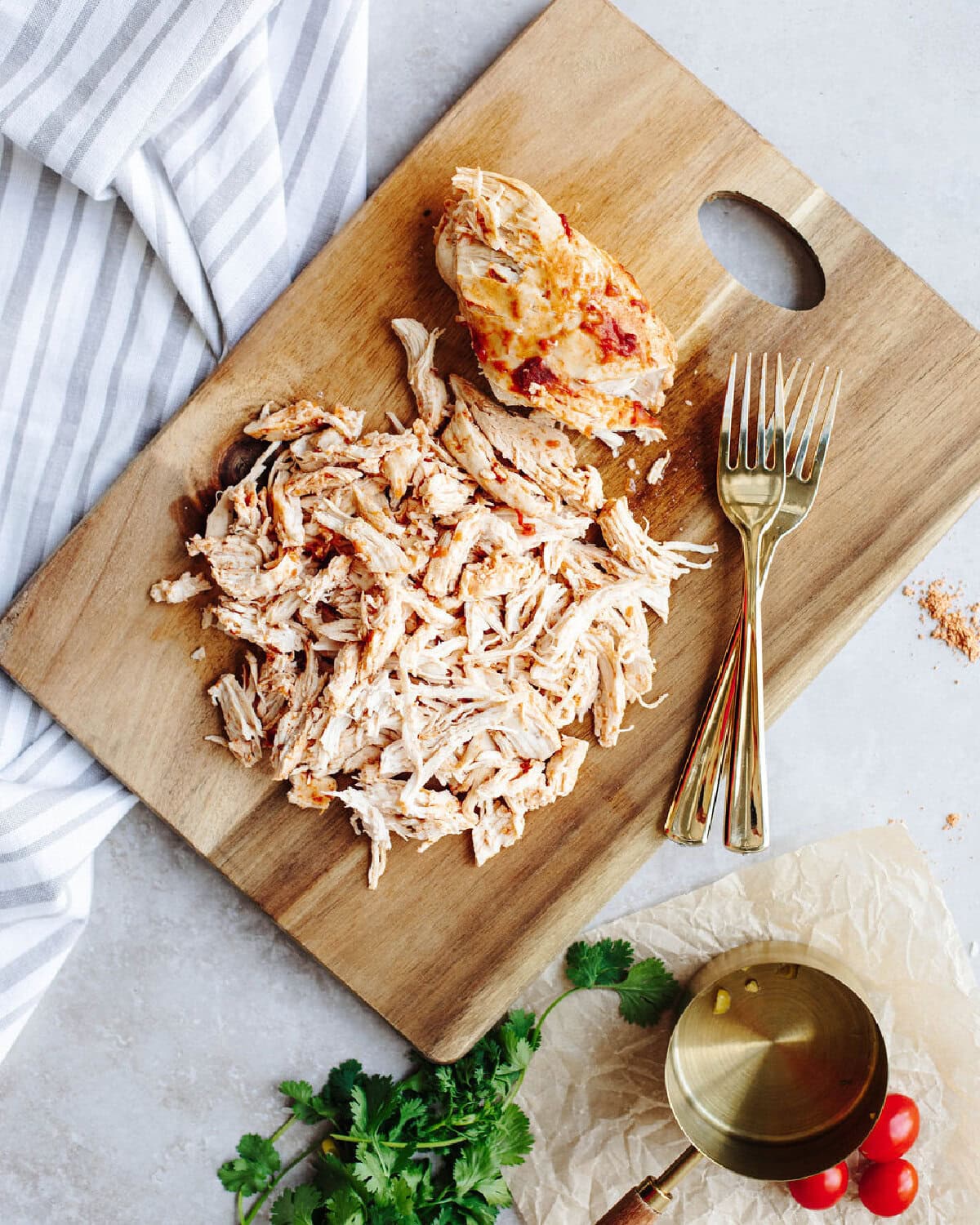 Cooked chicken shredded on a wood cutting board using two forks.