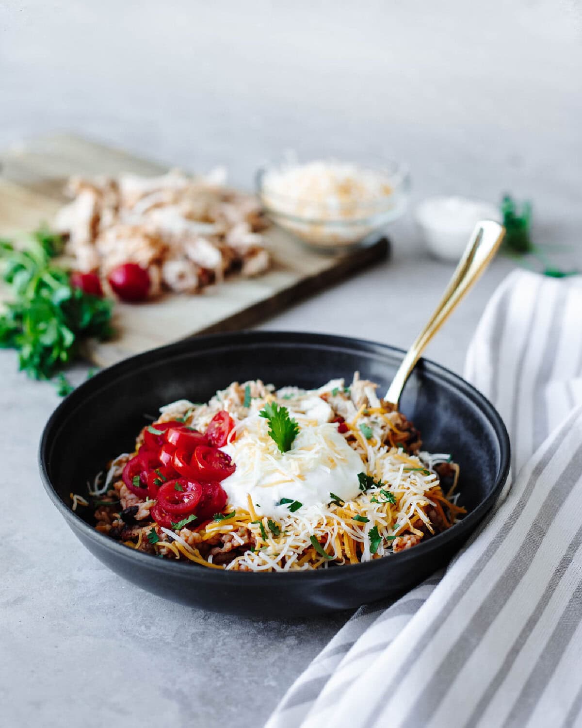 A black bowl with chicken taco bowls inside topped with sour cream and tomatoes.