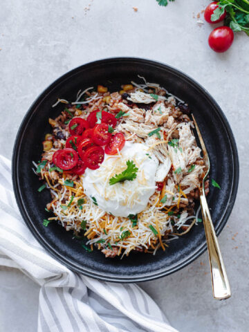 Chicken taco bowls served in a black bowl with sour cream, cheese, tomatoes, and cilantro.