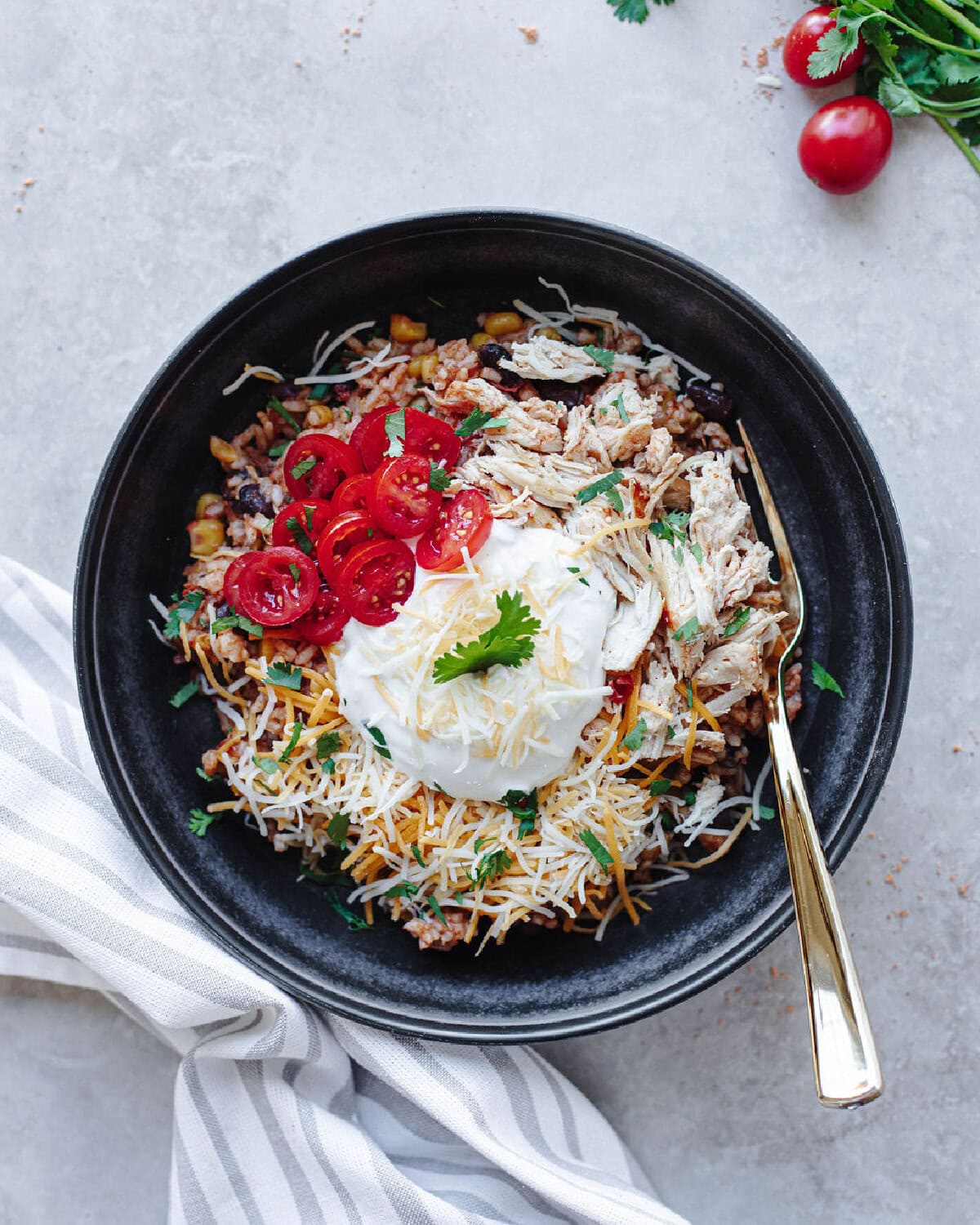 Chicken taco bowls served in a black bowl with sour cream, cheese, tomatoes, and cilantro.