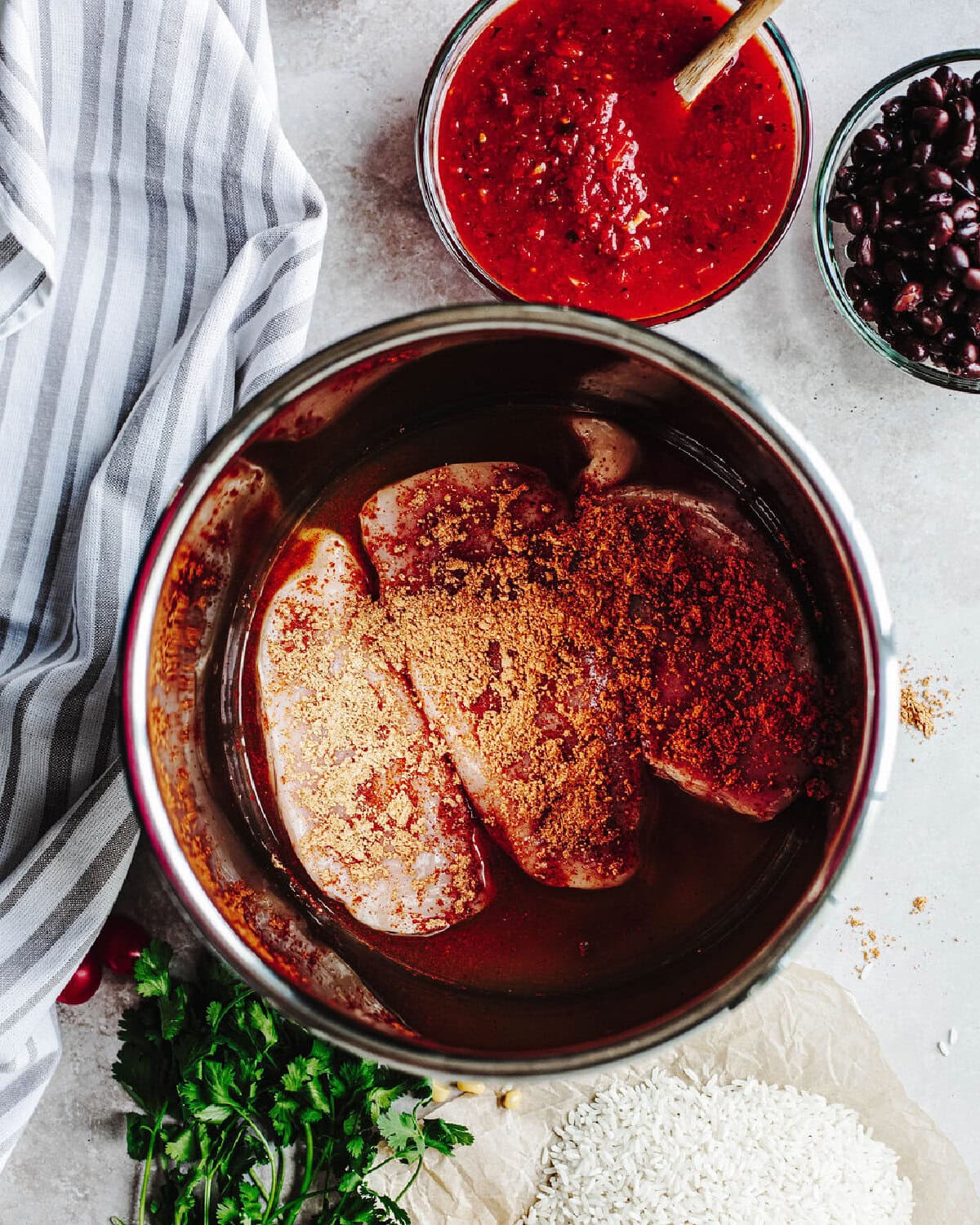 Chicken breasts topped with taco seasoning placed in a pressure cooker to cook with chicken broth.