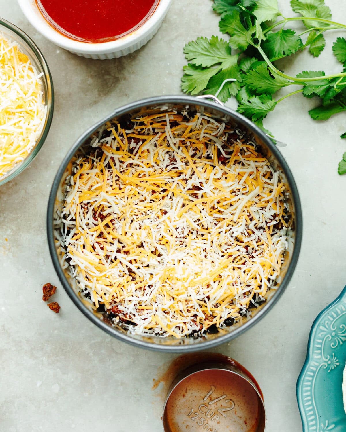 Shredded cheese sprinkled on top of layered tortillas and ground beef in a spring form pan.