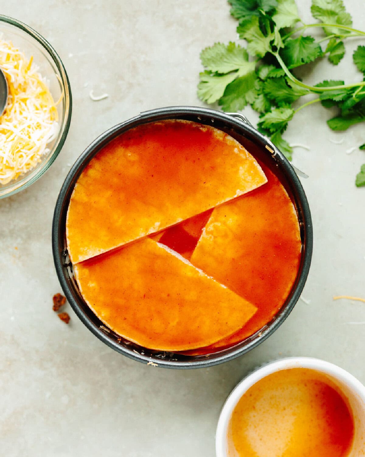 Red enchilada sauce poured on top of tortillas, cheese, and seasoned ground beef to form a casserole.