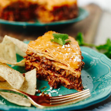 A slice of instant pot enchilada casserole served on a plate with some tortilla chips.