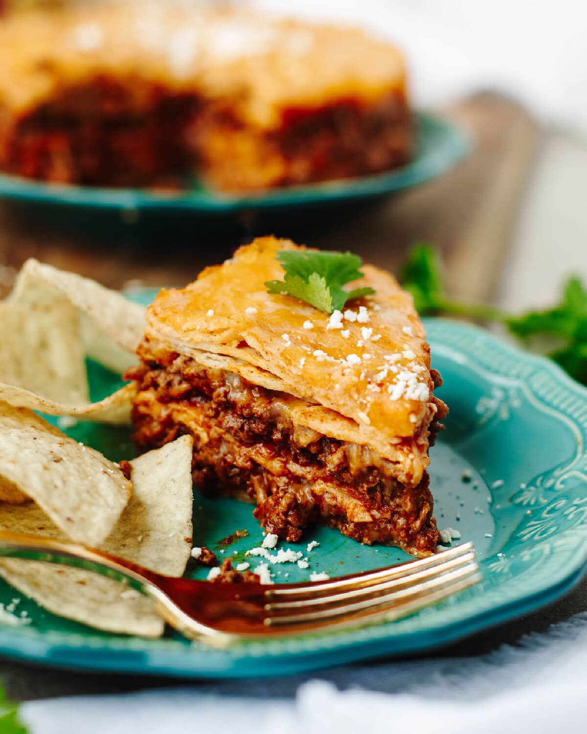 A slice of instant pot enchilada casserole served on a plate with some tortilla chips.