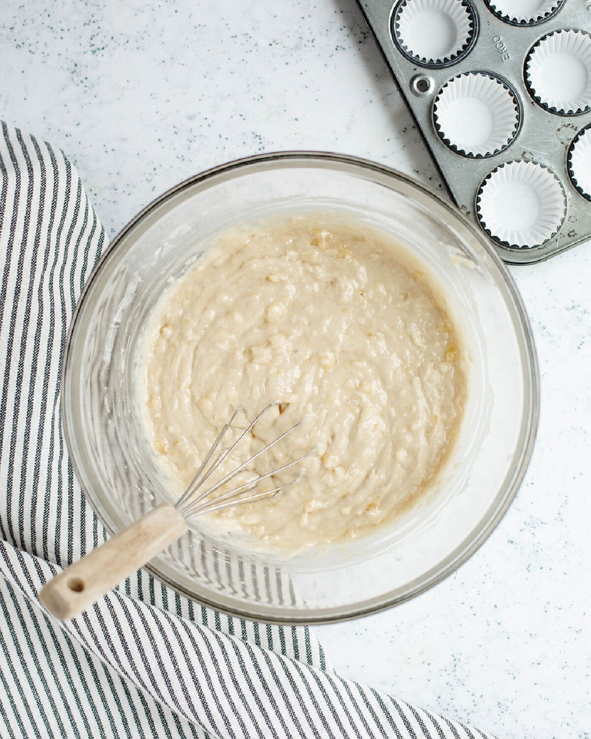 A dry flour mixture folded into the wet banana ingredient mixture in a glass mixing bowl.