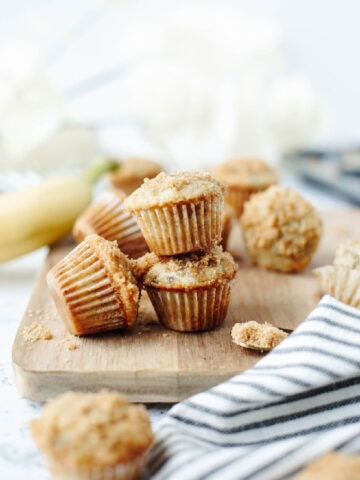 A stack of baked mini cinnamon banana muffins on a wood serving board.