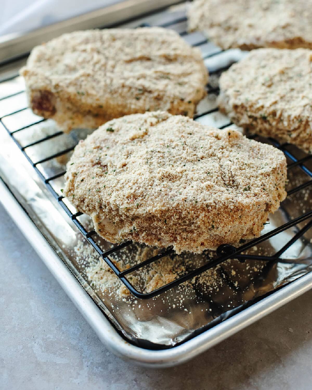 Breaded pork chops on a wire rack ready for the oven.