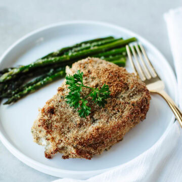 Ranch coated pork chop baked and served on a white plate with a serving of asparagus.