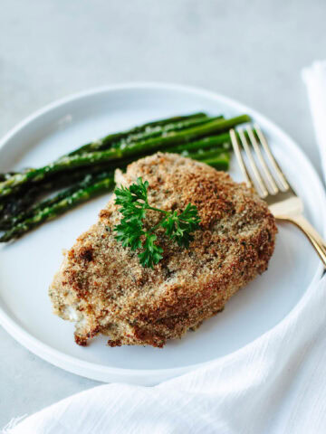 Ranch coated pork chop baked and served on a white plate with a serving of asparagus.