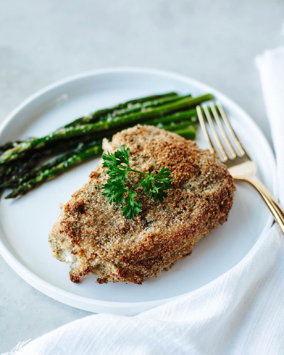 Ranch pork chop baked and served on a white plate with a serving of asparagus.